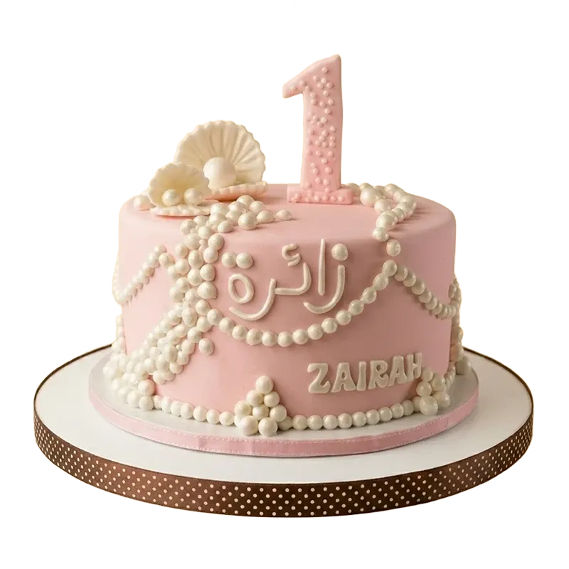 Pink first birthday cake with pearl strand draping, pearl clusters, clam shell, and name inscription