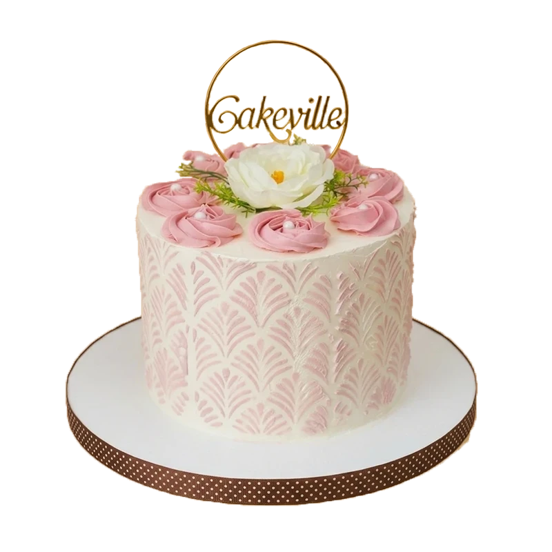 Pink floral stencil cake with pink rosettes, white peony, and gold Cakeville hoop topper