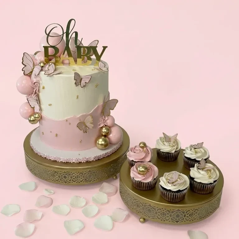 Two-tier pink baby shower cake with Oh Baby topper, gold butterfly decorations, and matching cupcakes