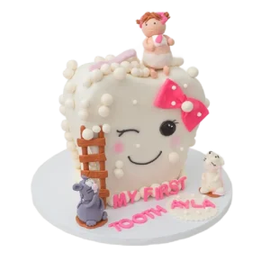 First tooth celebration cake shaped as smiling tooth with pink bow, baby girl, and mouse figurines