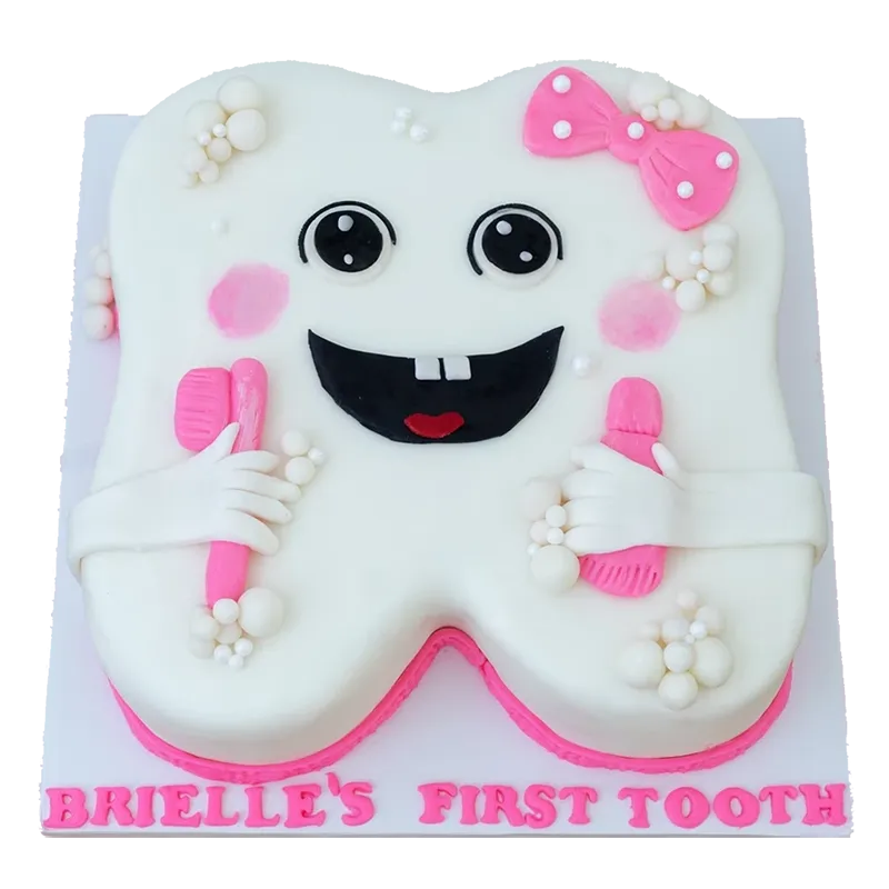 White tooth-shaped first tooth cake with pink bow, smiley face, and pink toothbrushes
