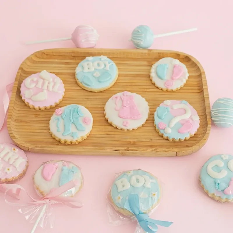 Gender reveal cookies with Boy and Girl text in pink and blue baby clothing designs with cake pops
