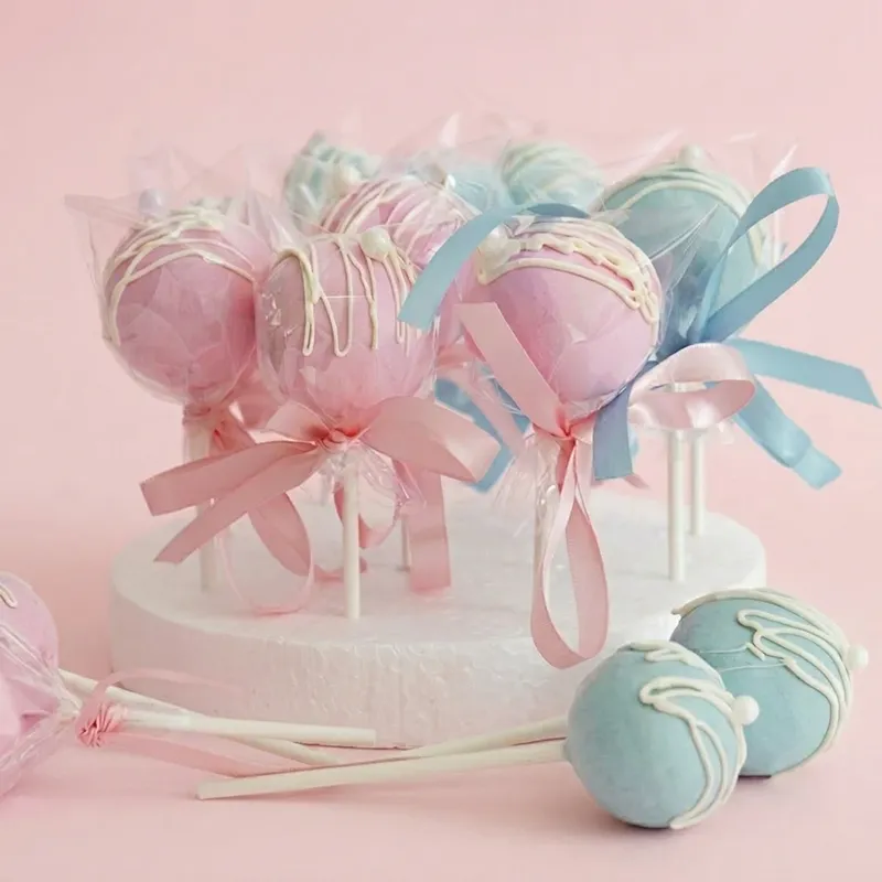 Sweet Suspense gender reveal cake pops in pink and blue with white drizzle and ribbon bows