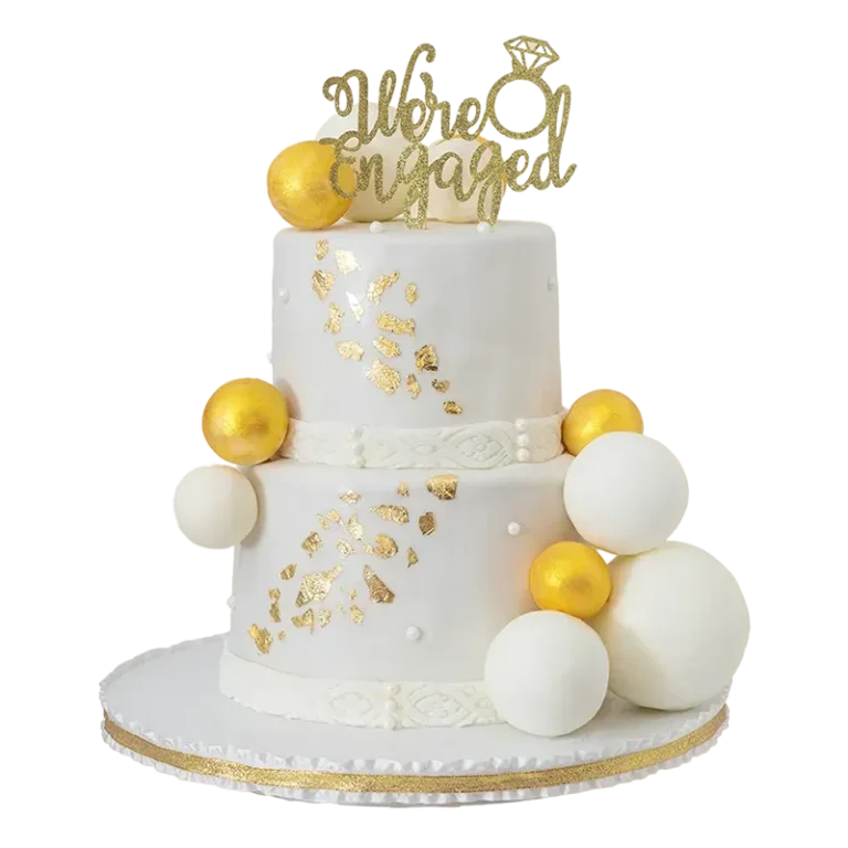 Two-tier white engagement cake with gold leaf, gold spheres, and We're Engaged topper