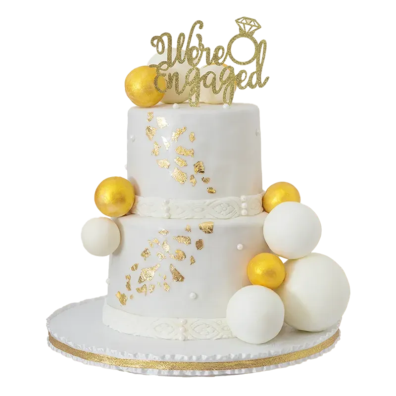 Two-tier white engagement cake with gold leaf, gold spheres, and We're Engaged topper