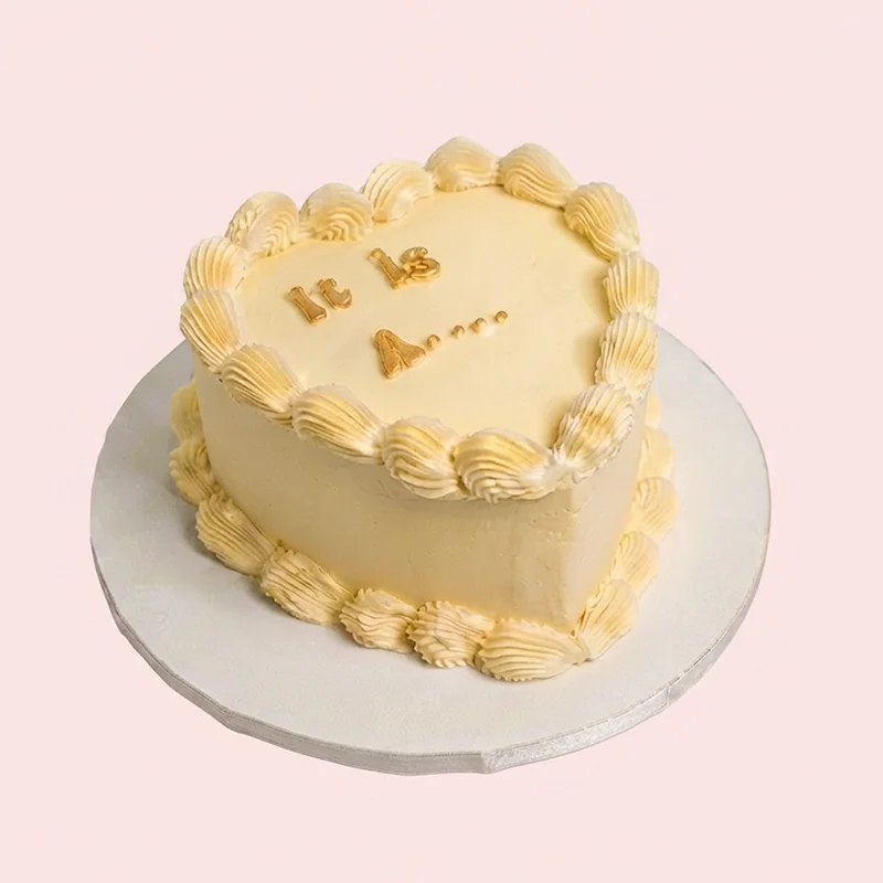 Buttercream yellow heart shaped gender reveal cake with shell piping and gold lettering by Cakeville Scarborough