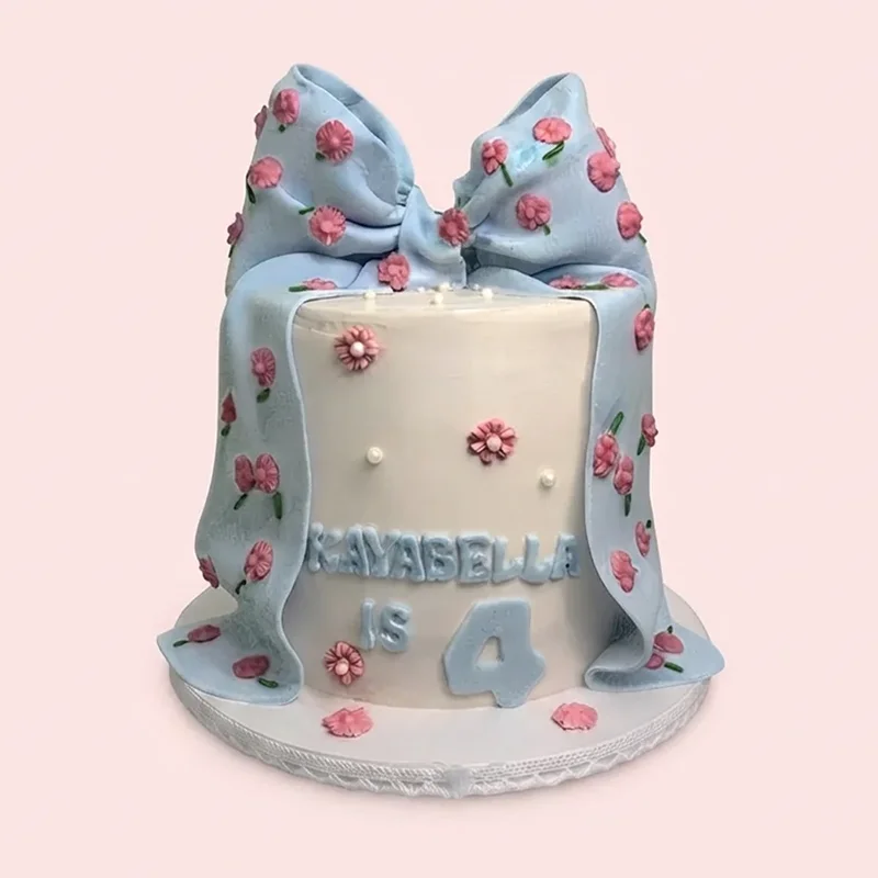 White and blue birthday cake with draped fondant bow and pink flowers by Cakeville Scarborough