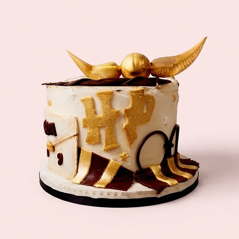 Cream and gold wizard themed birthday cake with winged ball topper and scarf detail by Cakeville Scarborough