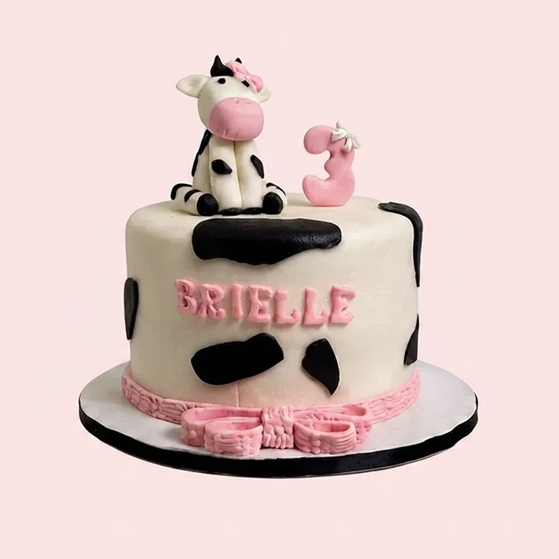 White cow print birthday cake with fondant cow figure and pink accents by Cakeville Scarborough